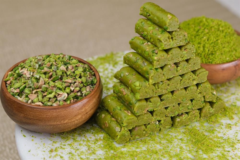 Green pistachio cookies stacked in a pyramid with a bowl of chopped pistachios and ground pistachios on a light background.